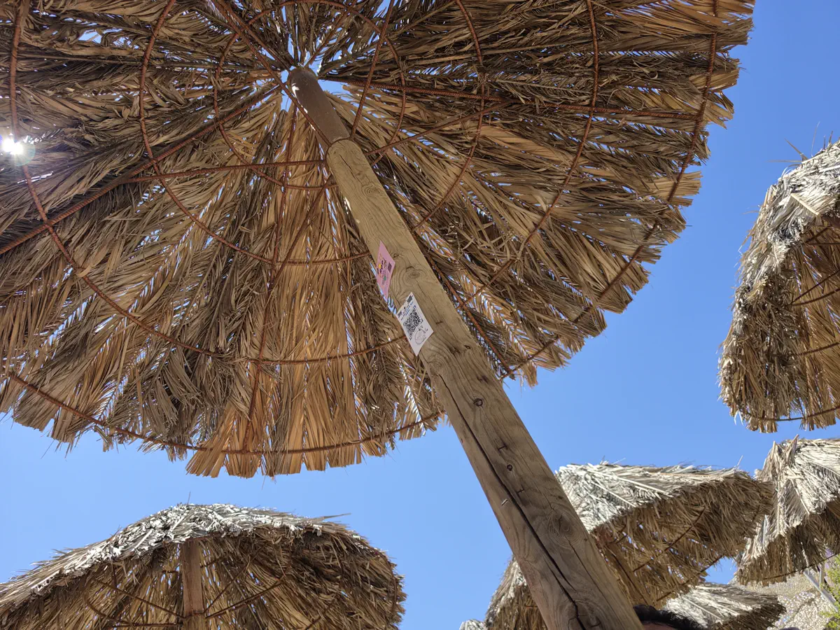 Straw beach parasols photographed from directly underneath against a clear blue sky